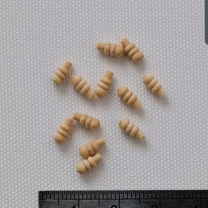 May include: A close-up of a ruler measuring 15cm, with 32 small markings between each centimetre.  There are 12 small wooden pieces scattered on a white surface.  The pieces are about 2.5cm long and are shaped like small, twisted logs.