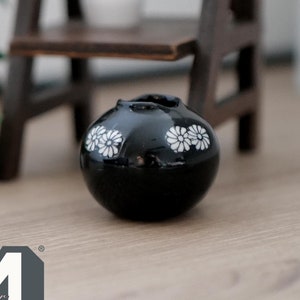May include: A small black ceramic vase with white floral designs. The vase is round and has a wide mouth.
