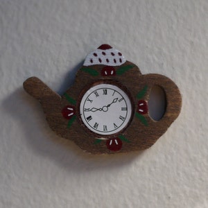 May include: A wooden teapot clock with a white face and black Roman numeral markings. The teapot is painted with red and green details and has a white and red lid.