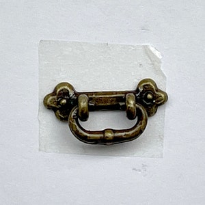 May include: A small, antique-style, brass door pull with a decorative design. The pull is about 2 inches long and has a simple, elegant design.
