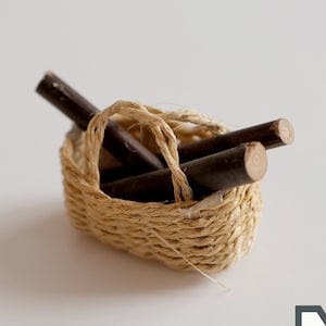 May include: A small woven basket filled with brown wooden sticks. The basket is made of natural materials and has a rustic look.