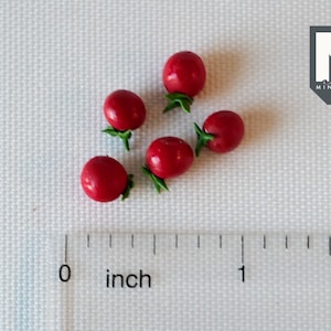 May include: Six miniature red tomatoes with green stems, arranged on a white surface with a ruler showing 1 inch.
