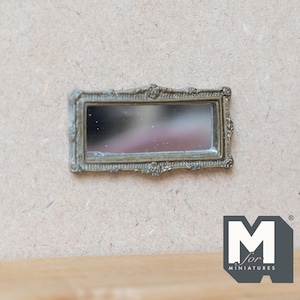 Pode incluir: Um espelho miniatura de cor prateada adornado com uma moldura retangular. O espelho está montado numa parede de cor castanho claro.