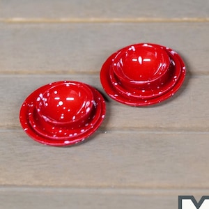 May include: A set of three red and white speckled miniature dishes. The dishes are stacked on top of each other. The dishes are on a wooden surface.