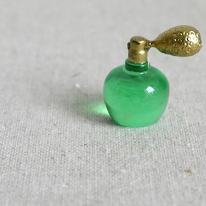 May include: A small, green glass bottle with a gold atomizer. The bottle is round and has a textured surface.