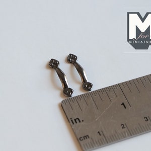 Può includere: Due piccole maniglie per ante di armadio in metallo nero, ciascuna misura circa 2,5 cm di lunghezza, sono mostrate accanto a un righello.