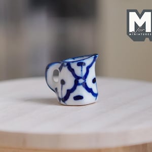 Peut inclure: Un pichet miniature en céramique bleu et blanc avec un motif traditionnel. Le pichet est posé sur une table en bois.