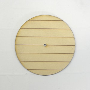 May include: A round, unfinished wooden craft piece with a series of horizontal lines, resembling planks. A small hole is centered. The wood has a light, natural color. Ideal for DIY projects and crafting.