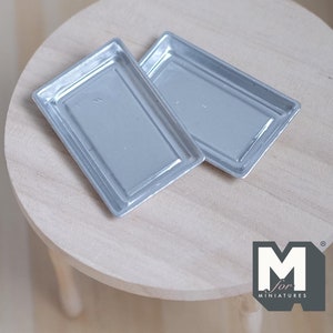 Könnte beinhalten: Zwei silberne Backbleche aus Metall, perfekt für Miniatur-Puppenhausküchen. Die Bleche sind rechteckig und haben einen leicht erhöhten Rand.