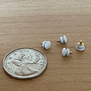 May include: Four white ceramic drawer knobs with gold metal hardware. The knobs are stacked in pairs and are about the size of a quarter.