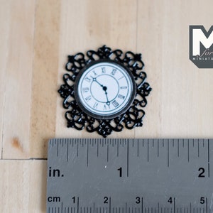 May include: Black metal clock face with Roman numerals and a black and white clock face. The clock is 1 inch in diameter and is shown next to a ruler.