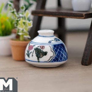 May include: A small, white ceramic vase with a blue and white floral design. The vase is decorated with a blue and white lattice pattern and a floral motif with pink and green accents.