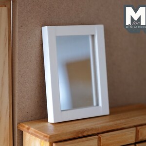 May include: White framed mirror with a reflective surface, sitting on a wooden dresser with multiple drawers.