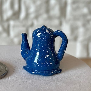 May include: A small blue ceramic teapot with white speckles. The teapot has a spout and a handle.