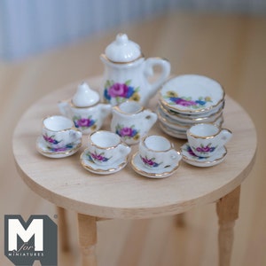 May include: A miniature porcelain tea set with floral designs. The set includes a teapot, creamer, sugar bowl, four teacups, and four saucers. The set is displayed on a small wooden table.