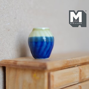 May include: A small blue and white ceramic vase with a striped pattern. The vase is sitting on a wooden shelf.