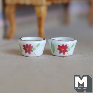 May include: Two small white ceramic bowls with red and green floral designs. The bowls have a gold rim and are perfect for miniature dollhouse decor.