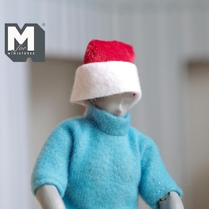 May include: A small doll wearing a blue sweater and a red and white Santa hat.