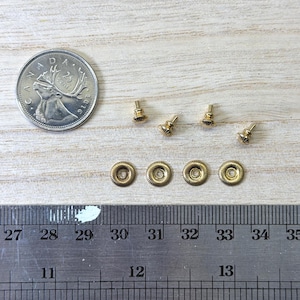 May include: Four small gold-toned metal rivets with a circular, ridged design, accompanied by four matching screw-back posts. A Canadian 25-cent coin and a metal ruler are included for scale, showing the components are approximately 0.25 inches wide.