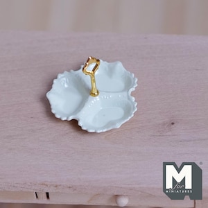 Può includere: Un piccolo piatto da portata azzurro a tre scomparti con manico dorato. Il piatto ha un bordo smerlato ed è progettato per uso in miniatura. Il logo "M for miniatures" è visibile in basso a destra.