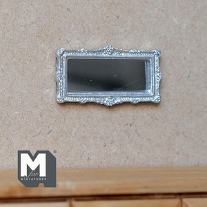 May include: A silver, ornate, rectangular mirror with a beveled edge. The mirror is mounted on a light brown wall.
