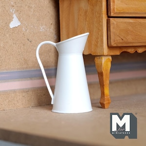 May include: White metal jug with a handle, sitting on a wooden surface. The jug is approximately 15 cm tall.