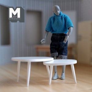 May include: Two white miniature round tables with three legs each. A mannequin wearing a blue sweater and denim shorts stands nearby. The logo "M for MINIATURES" is in the upper left corner.