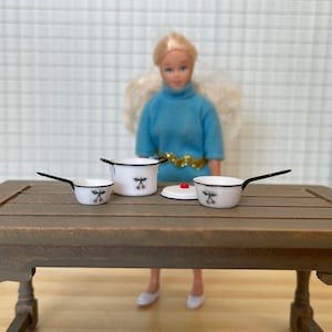 May include: Set of four miniature white enamel pots with black rims and a cherry design. The pots are on a wooden table.