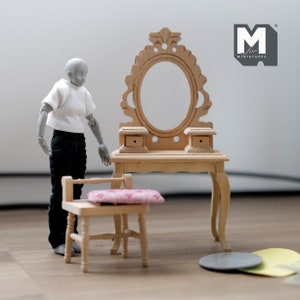 May include: A wooden vanity set with a mirror, two drawers, and a chair. The vanity is painted in a light wood colour and has a carved design on the mirror frame. The chair has a pink cushion. The set is designed for miniature dolls.