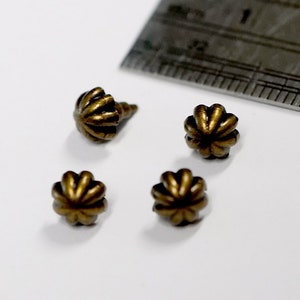 May include: Four antique gold-toned metal decorative nail heads with a scalloped design. The nail heads are approximately 1.2 cm in diameter and are shown next to a ruler for scale.
