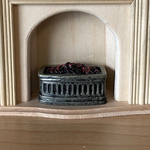 Può includere: Un camino per case di bambole in legno con un focolare in metallo nero e grigio. Il camino ha un design semplice con un arco arrotondato e un camino in legno.