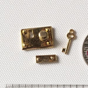 Op de afbeelding: Een miniatuur slot- en sleutelset in goudkleur met een klein, rechthoekig grendel. De set is ongeveer zo groot als een Canadese 25-cent munt.