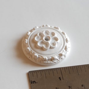 May include: White decorative ceiling medallion with a floral design. The medallion is approximately 2.5 cm in diameter.