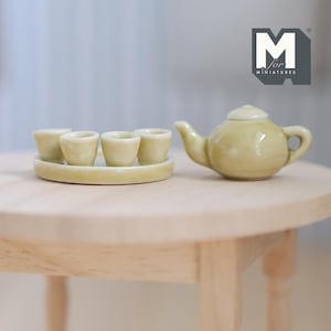 May include: A miniature tea set with a teapot and four cups on a round tray. The set is made of light green ceramic and is sitting on a wooden table.