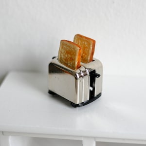 May include: A miniature silver toaster with two slices of bread popping up.