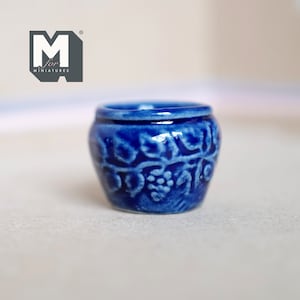 May include: A small blue ceramic pot with a vine and grape design. The pot is about 2 inches tall and is perfect for miniature dollhouses or fairy gardens.