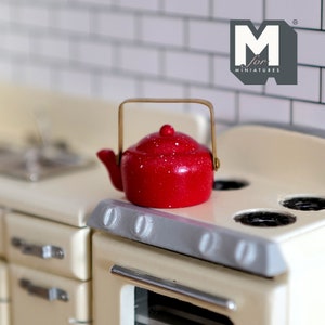 May include: Red miniature teapot with a gold handle sitting on a white stovetop with black burner rings. The stovetop has a silver trim. The teapot has white speckles on it. The text "M for Miniatures" is visible in the upper right corner of the image.