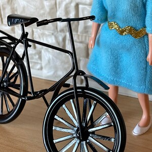 May include: A black metal bicycle with a white spoke wheel and a black seat. The bicycle is on a wooden surface.