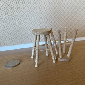 May include: Two wooden stools with a simple design, one is upright and the other is tipped over. The stools are made of light brown wood and have a round seat.