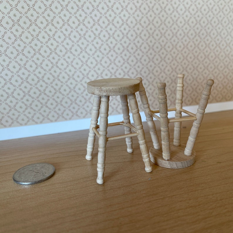 May include: Two wooden stools with a simple design, one is upright and the other is tipped over. The stools are made of light brown wood and have a round seat.