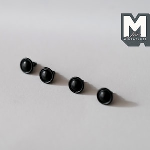 May include: Four black metal dome-shaped knobs with a small pin on the back. These knobs are commonly used for furniture or other decorative purposes.