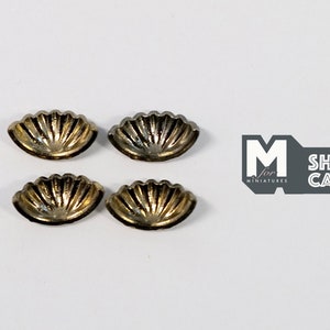 May include: Four gold-coloured metal seashell-shaped decorative pieces. Each piece has a scalloped edge and a ribbed design.