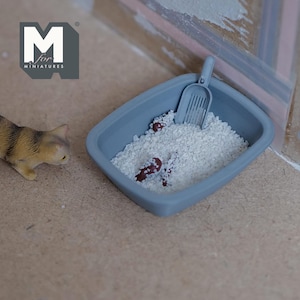 May include: A gray plastic litter box with white litter and a brown plastic scoop. There are three brown plastic cat droppings in the litter.