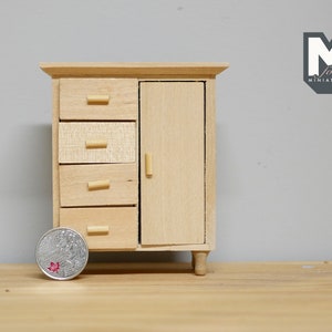 May include: A miniature wooden cabinet with four drawers and a single door. The cabinet is made of light wood and has a simple design. The cabinet is about the size of a coin.
