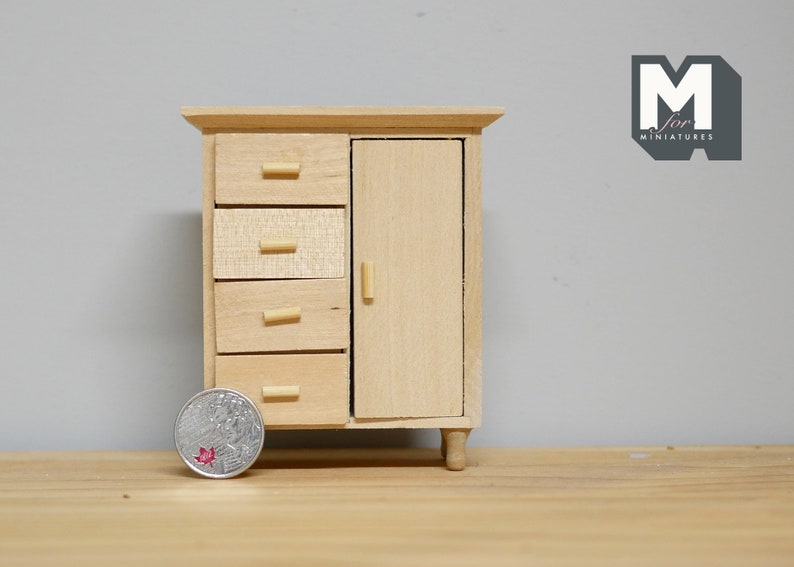 May include: A miniature wooden cabinet with four drawers and a single door. The cabinet is made of light wood and has a simple design. The cabinet is about the size of a coin.