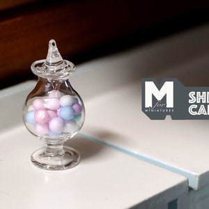 Könnte beinhalten: Eine klare Glasbonbondose mit Deckel und Fuß. Die Dose ist mit pastellrosa, blauen und weißen Bonbons gefüllt.