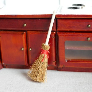 Op de afbeelding: Een miniatuur houten keukensets met een rode kast, een wit fornuis en een kleine bruine bezem met een rood lint.