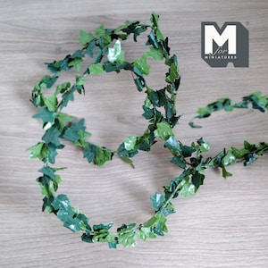 Könnte beinhalten: Eine grüne künstliche Efeugirlande mit unterschiedlich grünen Blättern. Die Girlande ist in einem Schleifenmuster auf einer Holzoberfläche angeordnet. Das Logo "M for Miniatures" ist oben rechts sichtbar.