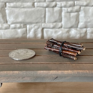 May include: A bundle of small, brown twigs tied together with black string. The twigs are arranged in a stack and are about the size of a quarter.