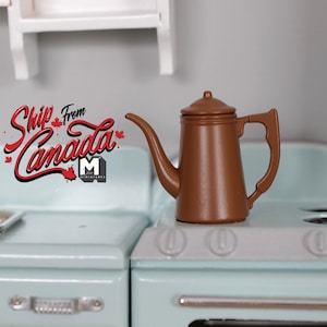 May include: A miniature brown coffee pot with a long spout and handle sits on a light blue toy stove. The stove has white accents and a silver handle. A white shelf is in the background.